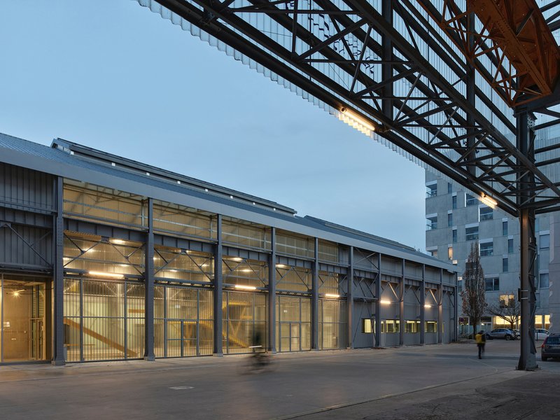 Exterior view of the glazed facade and steel canopy frame at twilight with interior lights glowing