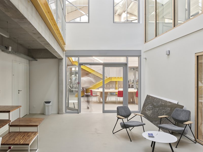 White-walled lobby space with concrete ceiling beam and glazed doors opening to a dining area beyond