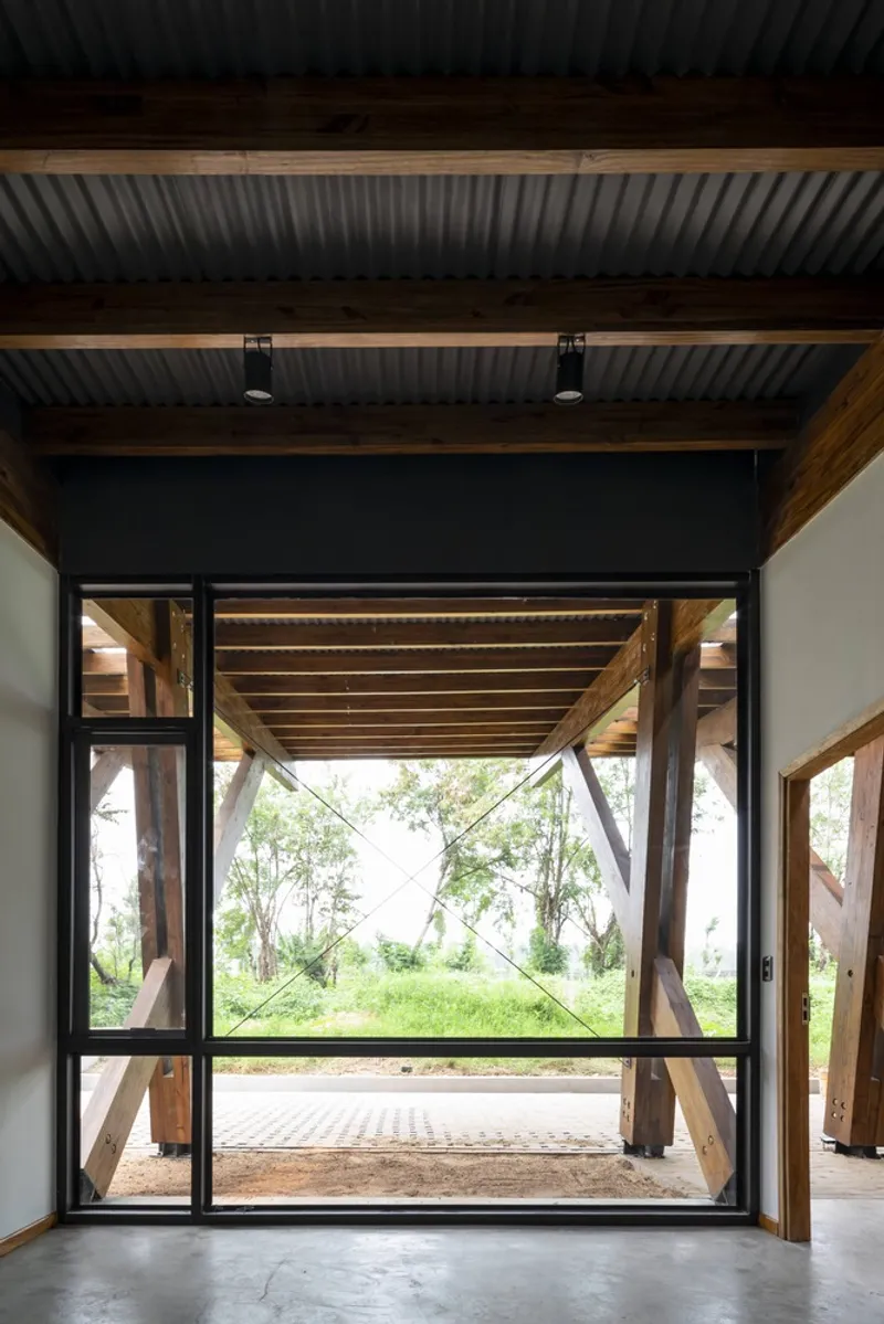 View through black-framed glass doors to covered terrace with exposed timber bracing and green field beyond