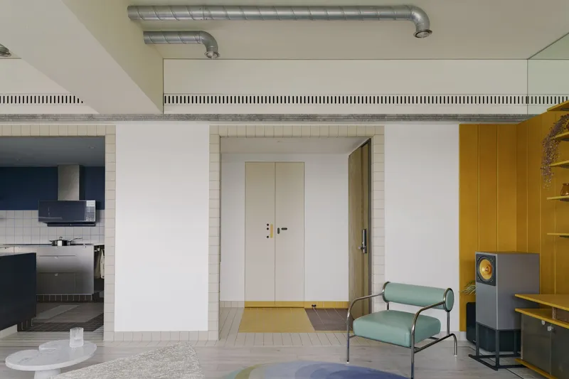 Open living area with exposed ductwork, white tile banding, and yellow millwork framing a doorway