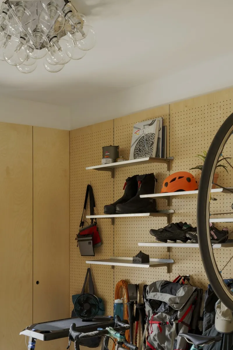 Pegboard wall with shelves holding cycling gear and helmets beneath a cluster of glass globe lights