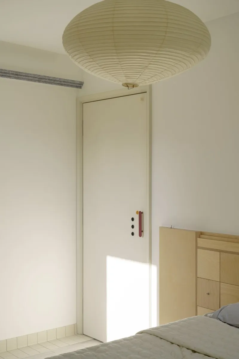 Bedroom door with maroon handle beneath a large pendant light casting sunlight across white walls