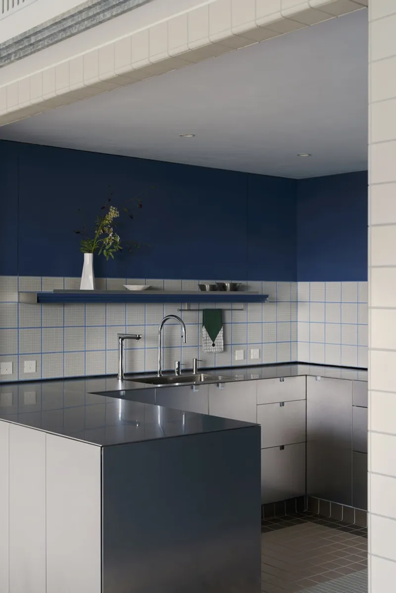 Kitchen island with stainless steel countertop beneath white square tile backsplash and navy blue upper wall