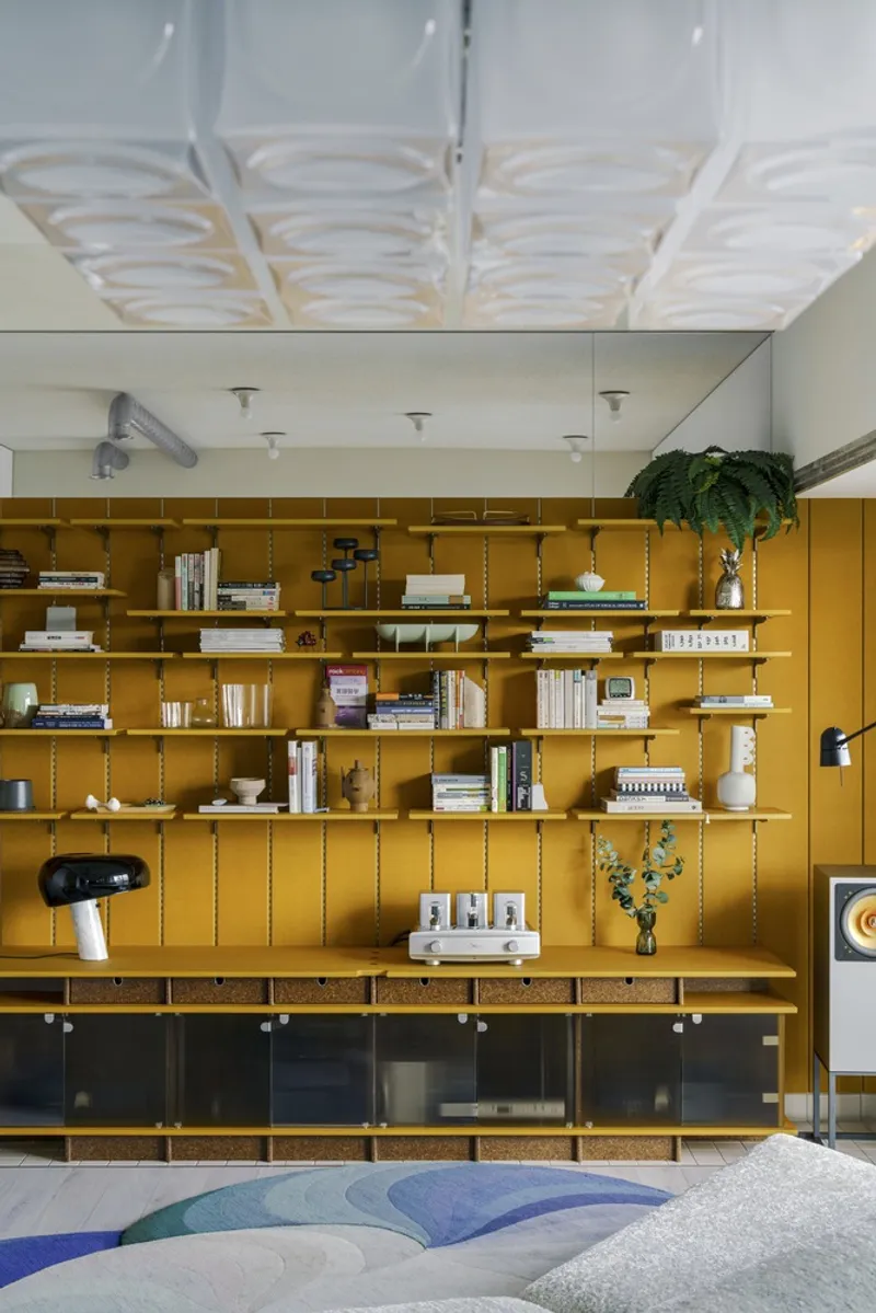 Mustard yellow shelving unit filled with books beneath an undulating white plaster ceiling