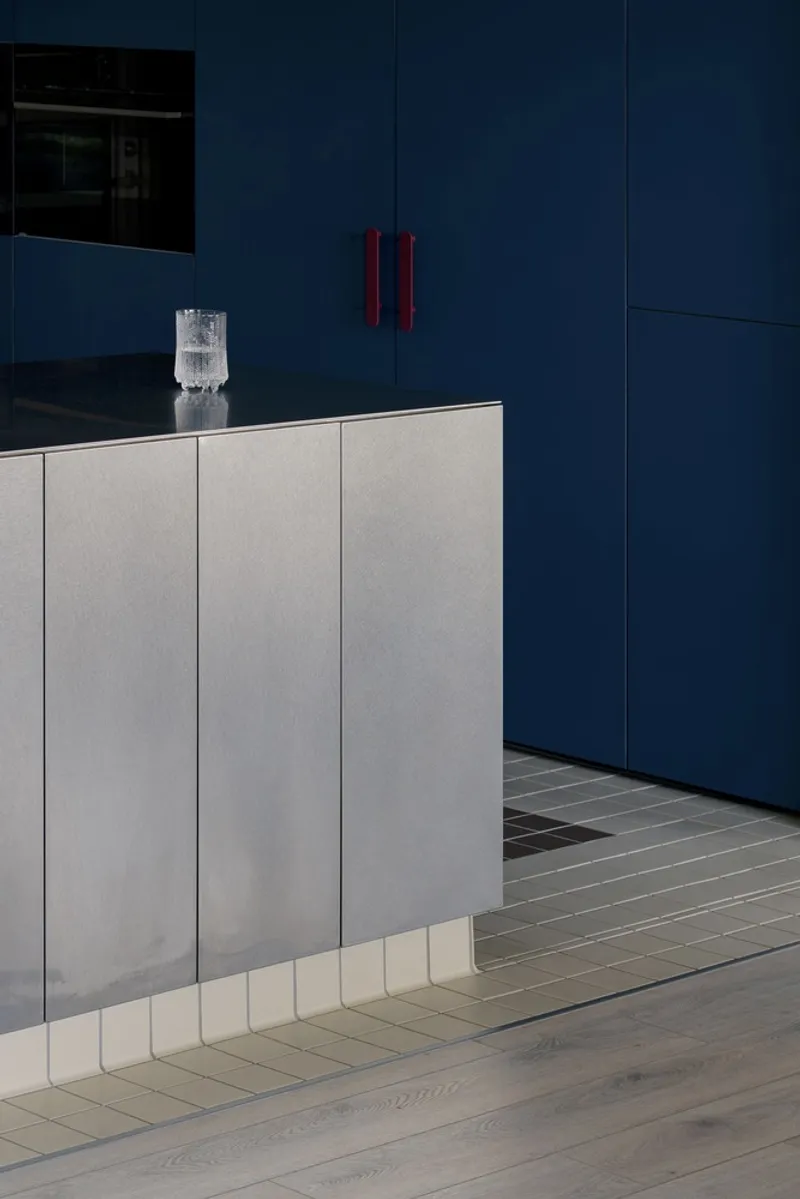 Grey laminate cabinetry base meets navy blue pantry doors with red vertical handles in soft light