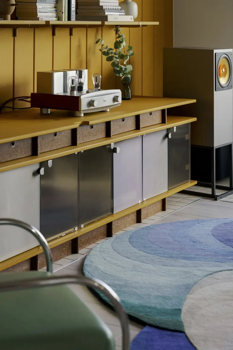 Close-up of the mustard-lacquered storage unit with sliding metal panels and cork dividers