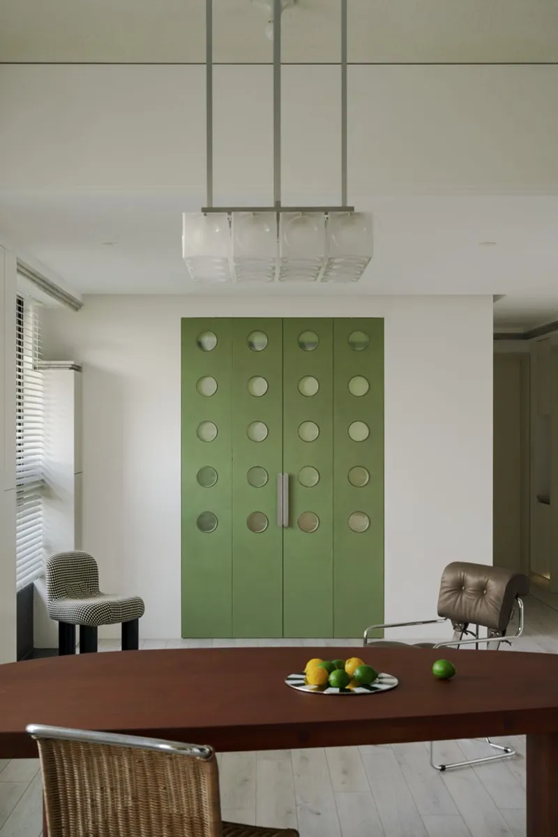 Olive green cabinet doors with circular recessed pulls beside a suspended glass pendant fixture