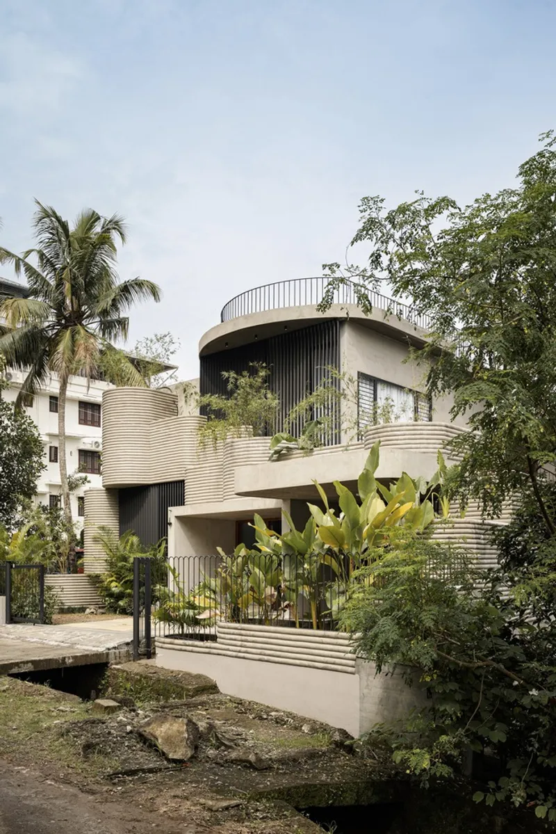 Curved facade with horizontal metal cladding and rooftop terrace surrounded by palms and tropical vegetation