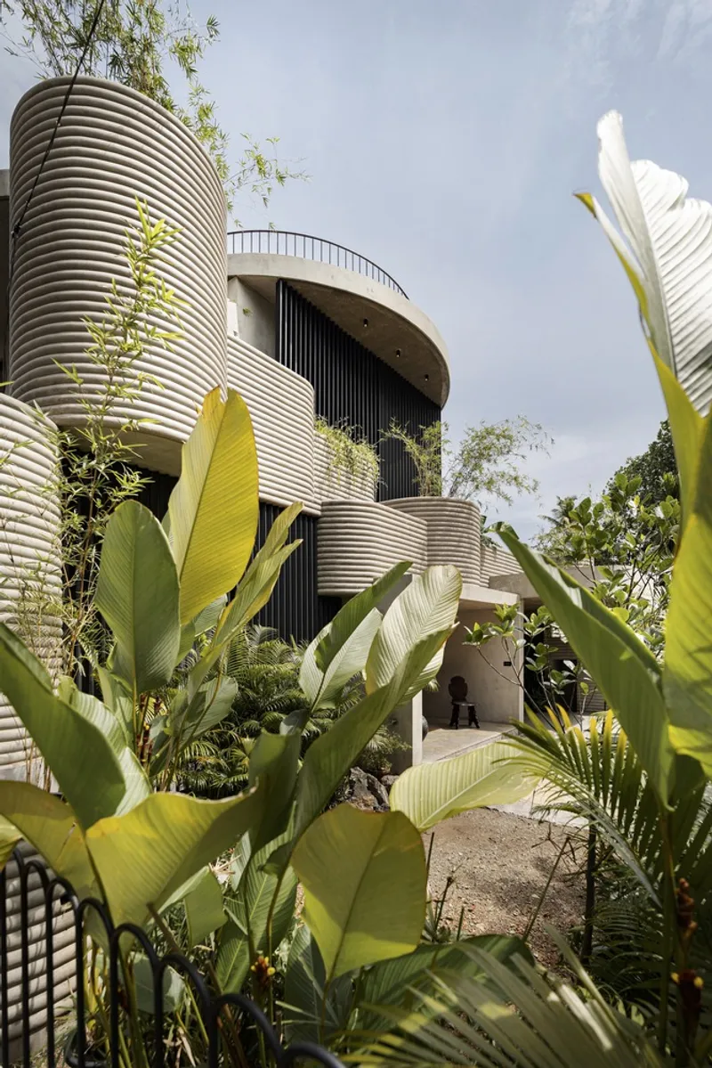 Stacked cylindrical towers with ribbed metal cladding framed by banana leaves in the foreground
