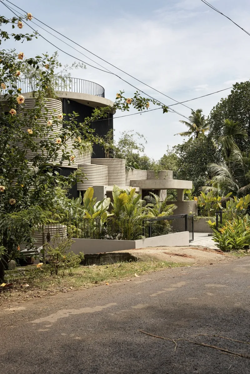 Street view of the cylindrical volumes with corrugated metal skin behind a low garden wall