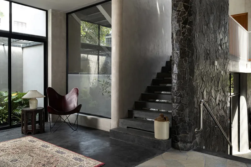 Entry foyer with concrete stair alongside textured stone wall and leather butterfly chair near glazed courtyard