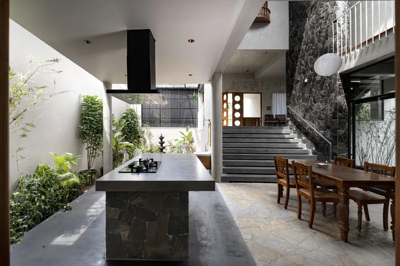 Open kitchen with dark marble island facing a stone staircase beside a planted courtyard