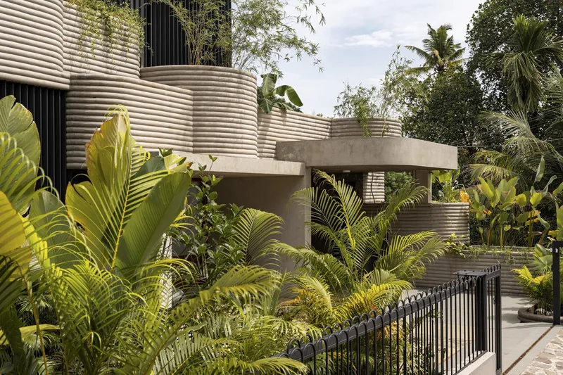 Street view of the ribbed metal facade and concrete canopy surrounded by banana leaves and tropical palms