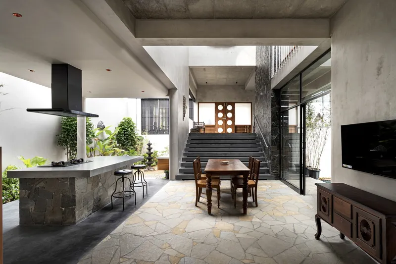 Open-plan living area with kitchen island, dining table and concrete stair beneath exposed ceiling beams