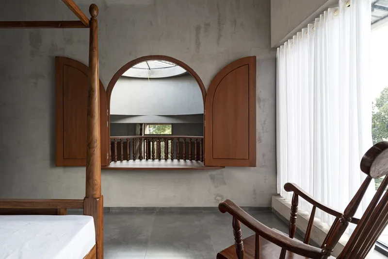 Bedroom interior with arched timber window opening to a balcony view of the atrium below