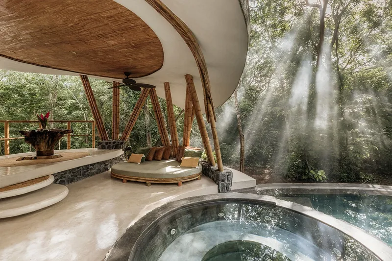 Interior view of circular pool beneath curved concrete shells and bamboo columns with mist beyond