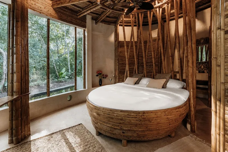 Bedroom with circular timber bed frame and diagonal bamboo columns framing corner windows