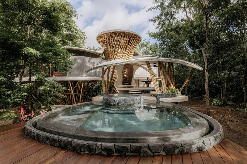 Concrete pool with radial steps leading to bamboo pavilion with latticed tower under partly cloudy skies