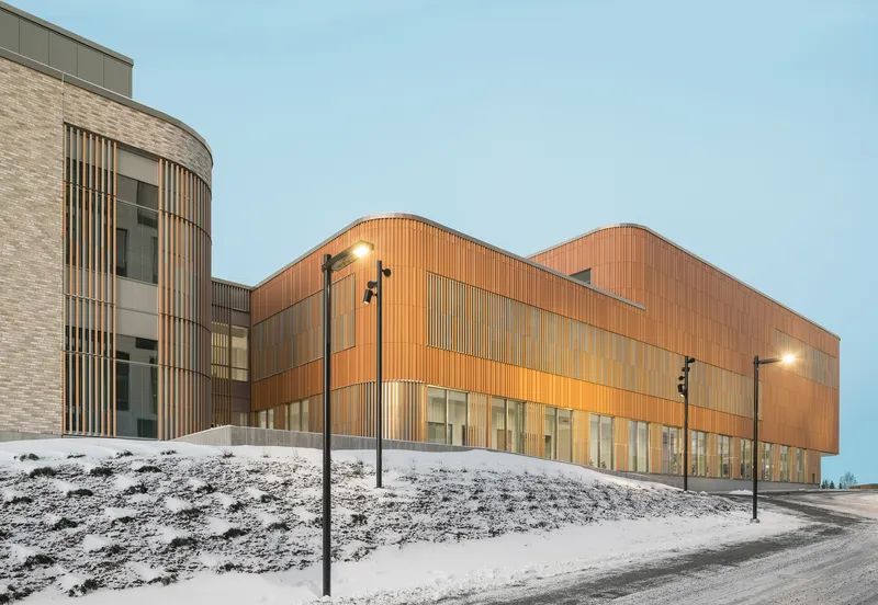 Wood-paneled volumes meeting brick wing on snowy slope under evening sky