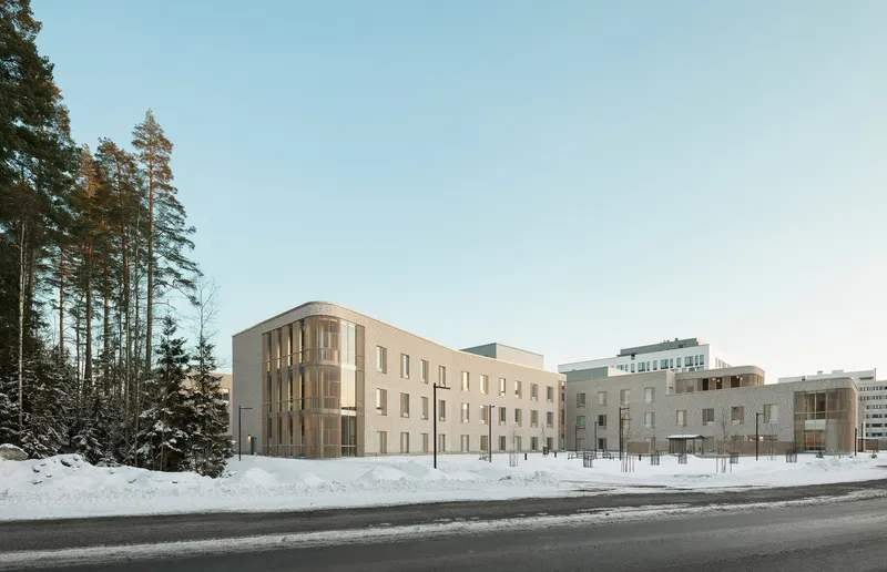 Street view of the brick facade with punched windows and vertical timber screening beside snow-covered pine trees