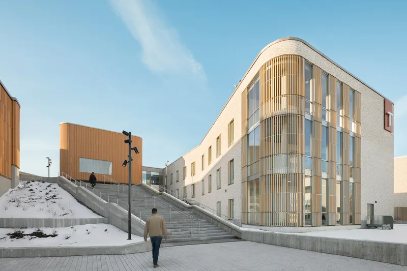 Curved corner volume with vertical timber slats and a pedestrian ascending the concrete staircase in winter