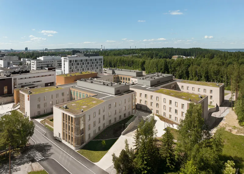 Aerial view of the low-rise courtyard buildings with green roofs surrounded by forest under summer clouds