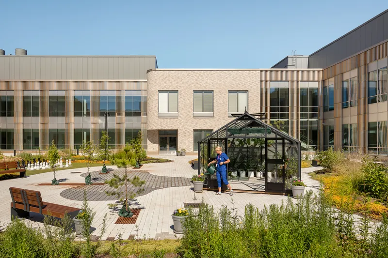 Central courtyard garden with glass greenhouse pavilion and planted beds between brick and timber-clad facades
