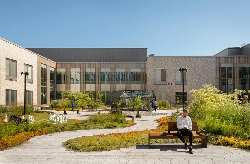 Courtyard garden with planted beds and paver paths between brick and timber-screened volumes under a clear sky