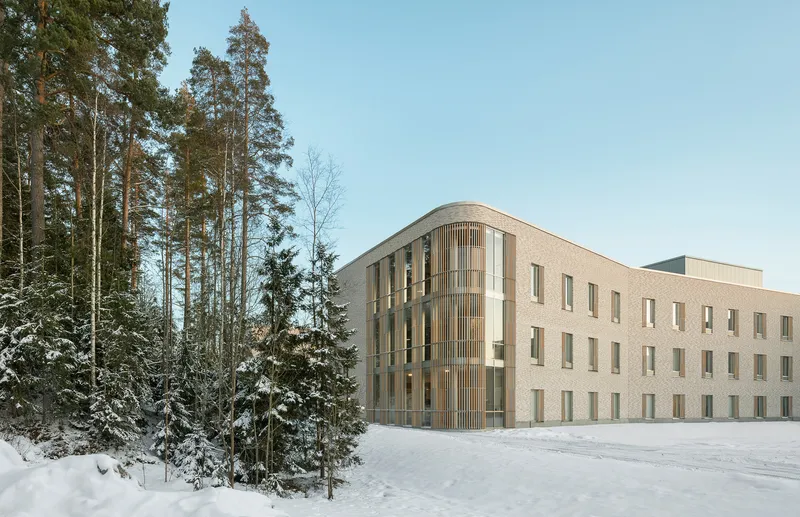 Brick facade with vertical timber screening and punched windows at the forest edge in fresh snow
