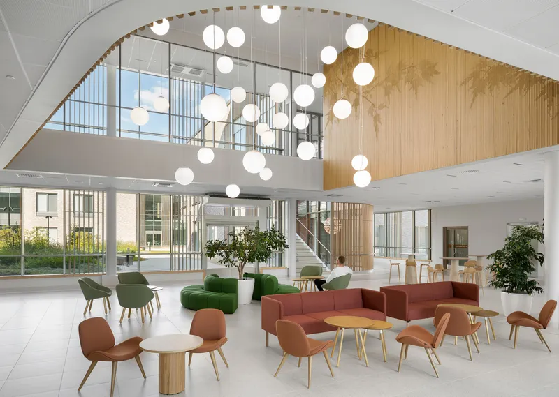 Double-height lobby with suspended globe pendants, curved timber wall, and mezzanine balcony above seating groups