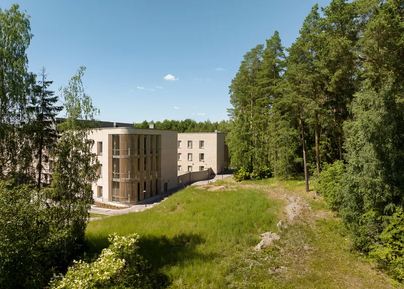 Aerial view of the curved brick volume nestled into a grassy hillside bordered by conifer forest