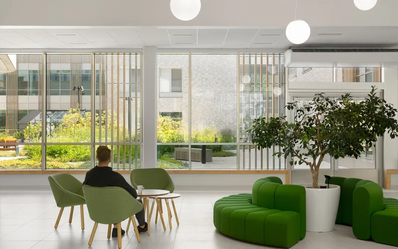 Common area with green upholstered seating and floor-to-ceiling windows overlooking the planted courtyard in daylight