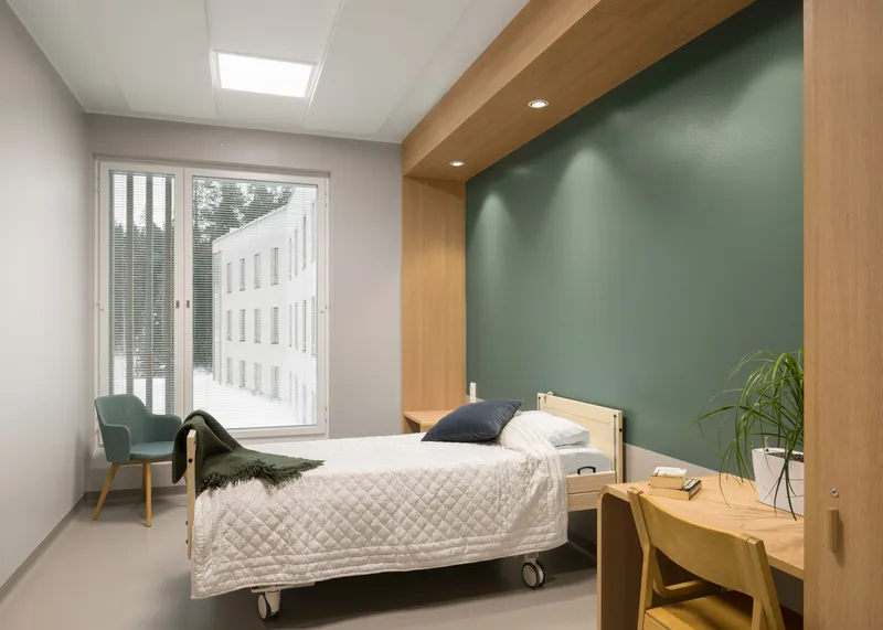 Bedroom with green accent wall, timber bulkhead, and a window overlooking the adjacent wing in summer