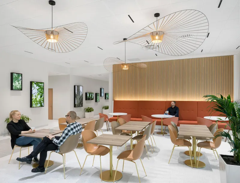 Cafeteria interior with spiral pendant lights, vertical wood slat wall, and orange banquette seating