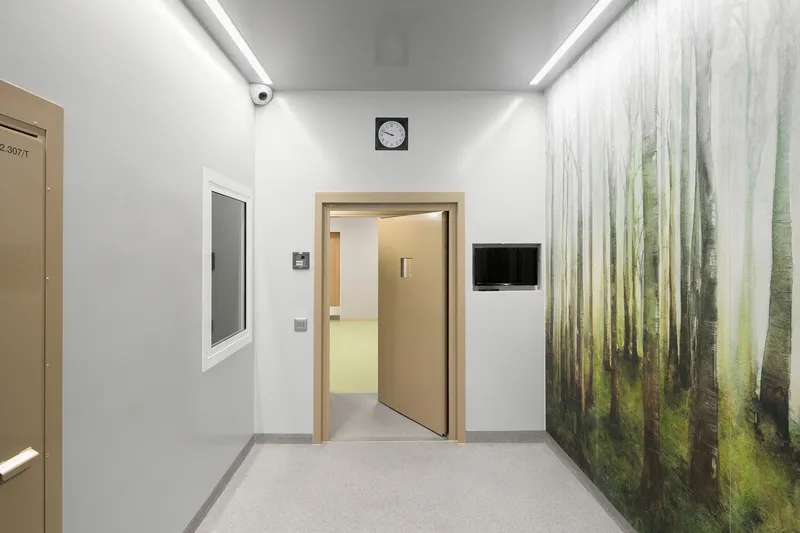 Corridor with wood-framed doorway, forest mural on right wall, and recessed cove lighting