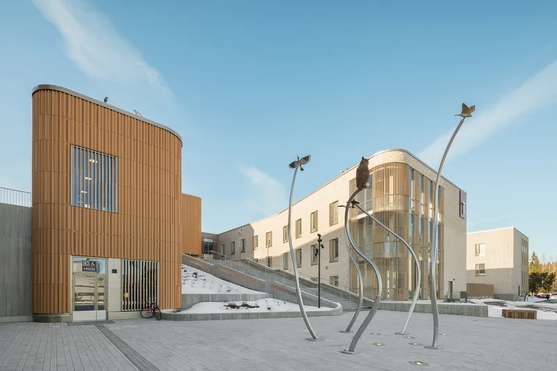 Exterior plaza with vertical wood cladding on curved volumes and sculptural metal bird installation
