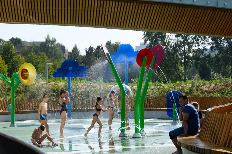 Splash pad with colorful flower-shaped water features beneath a timber slatted soffit