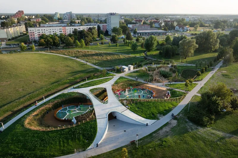 Drone view showing the white concrete pathways looping through planted beds and play zones at dusk