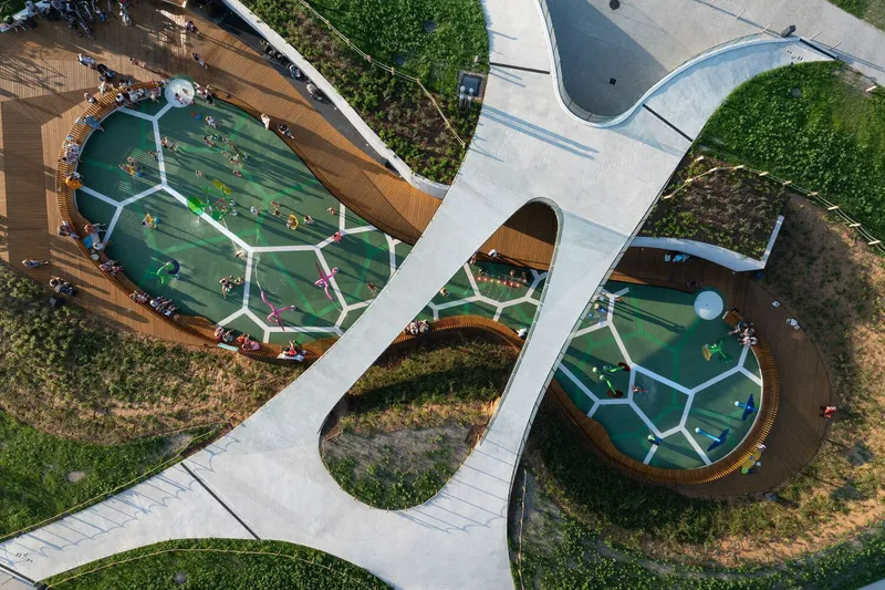 Top-down view of white concrete pathways weaving between circular play areas with timber edging