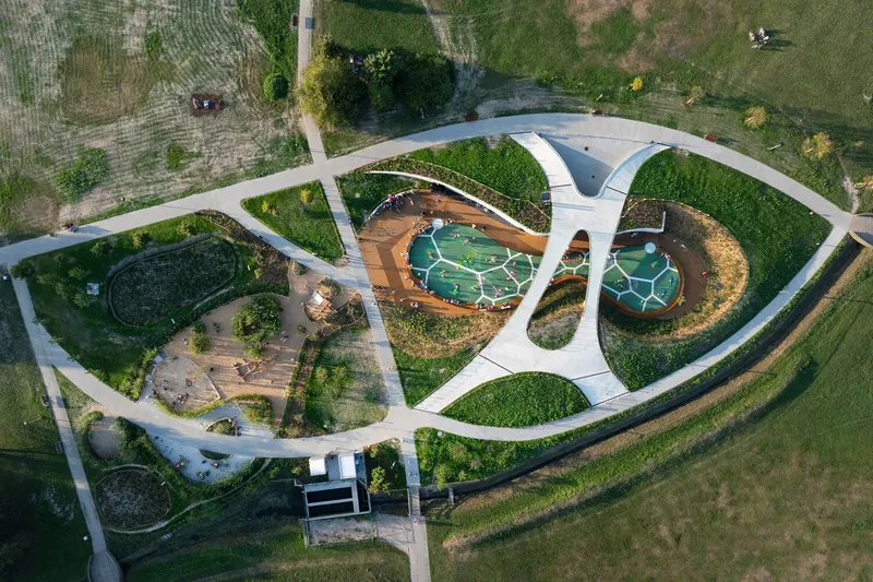 Aerial view of circular park layout with white pathways connecting play zones and planted mounds