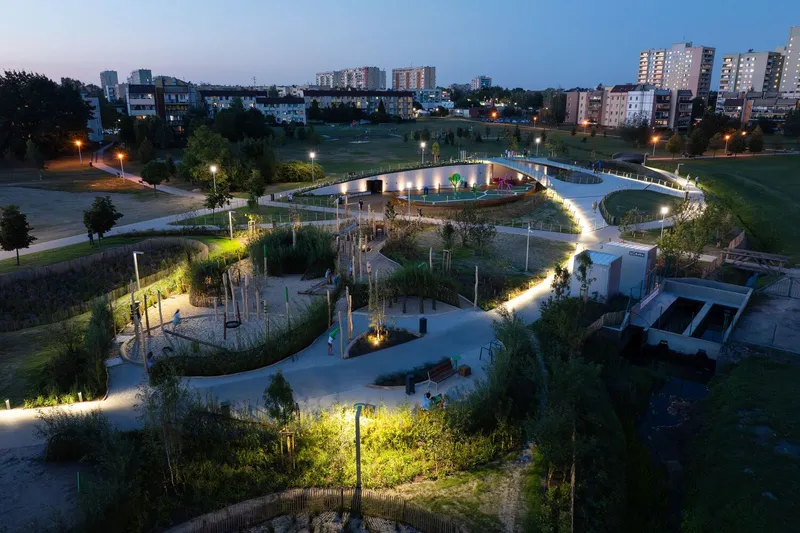 Aerial view of the spiraling pathways and planted zones illuminated at dusk with residential buildings beyond