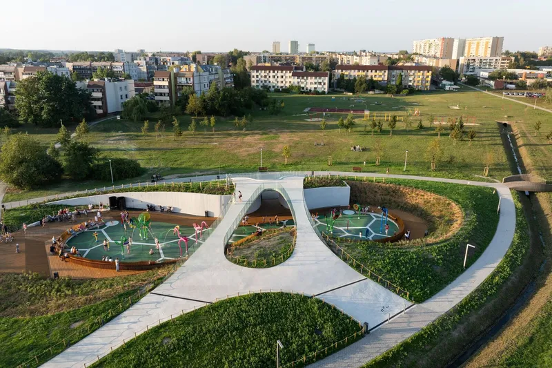 Aerial perspective of the concrete roof structure arching over play zones surrounded by planted berms