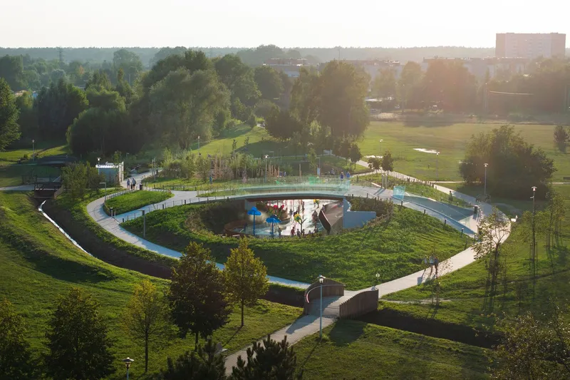 Elevated view of terraced park with spiral walkways surrounding sunken play area at golden hour