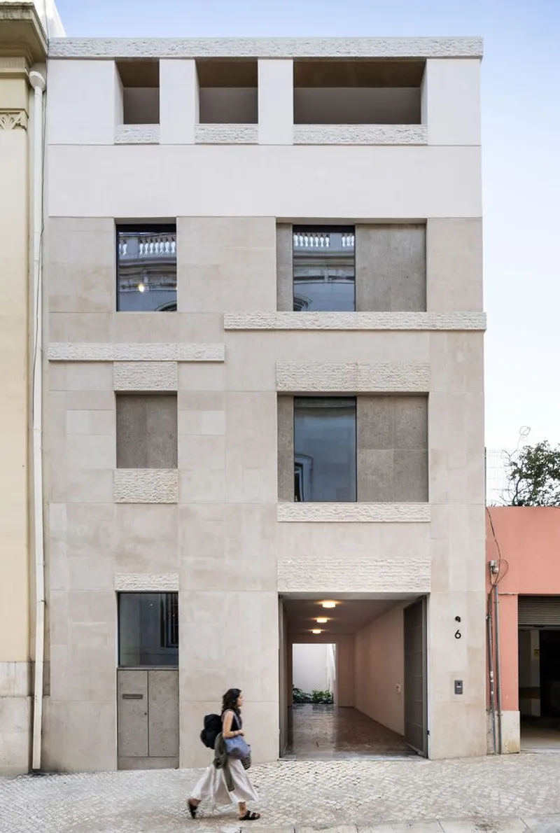 Street facade with stacked stone cladding and deep window reveals as a pedestrian passes below