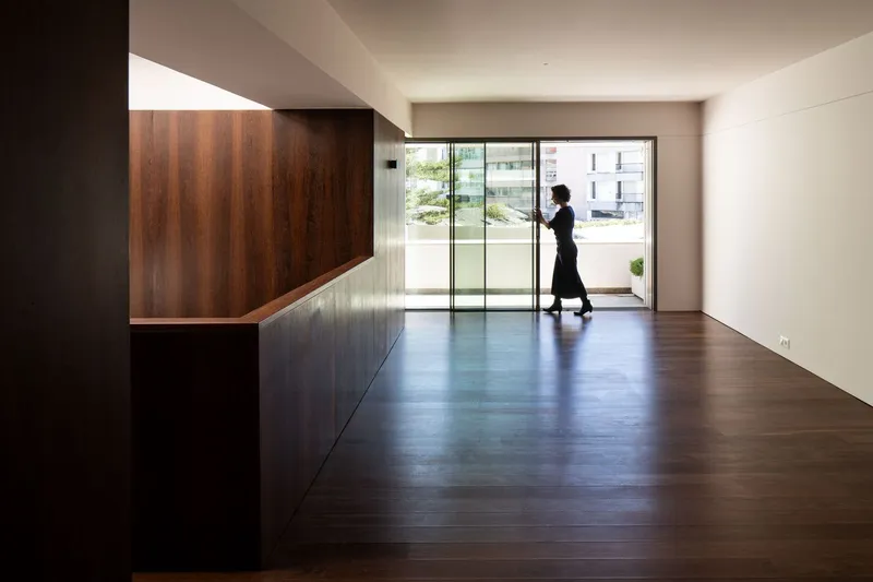 Open-plan interior with walnut millwork volume and timber flooring as a figure moves toward the glazing