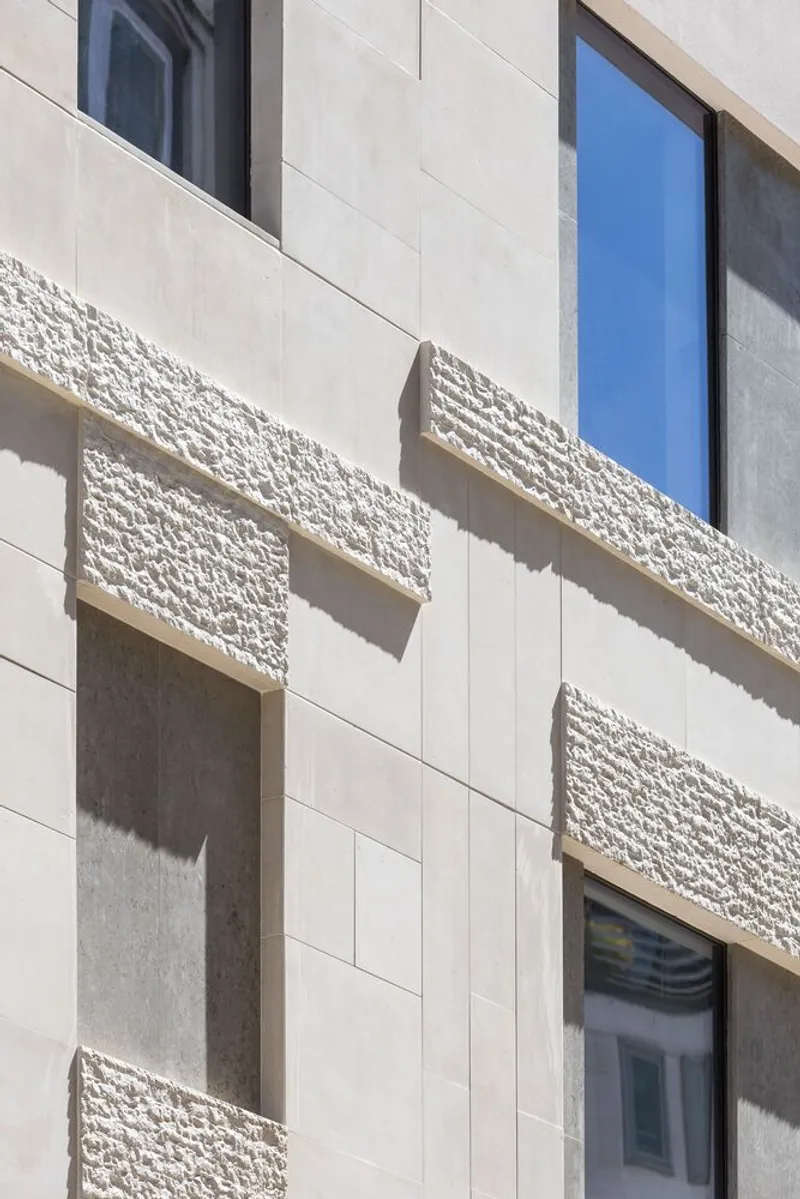 Facade detail showing recessed windows framed by textured stone panels under strong daylight