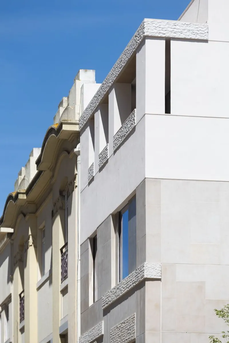 Street view of white facade with textured stone bands meeting an older masonry building