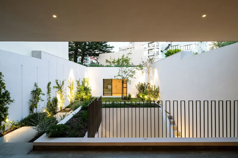 Courtyard with planted slope, uplighting, and vertical slat railing under cantilevered ceiling at dusk