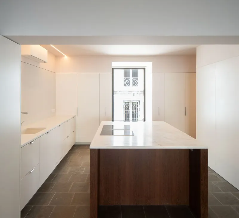 Kitchen with white cabinetry, dark wood island and stone floor facing window with balcony