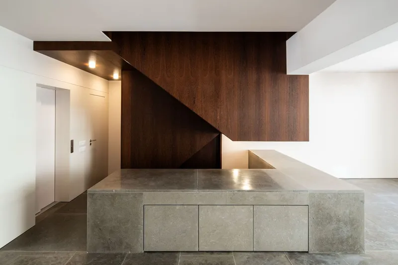 Entry hall with dark wood-paneled staircase and gray stone platform lit by recessed ceiling fixtures